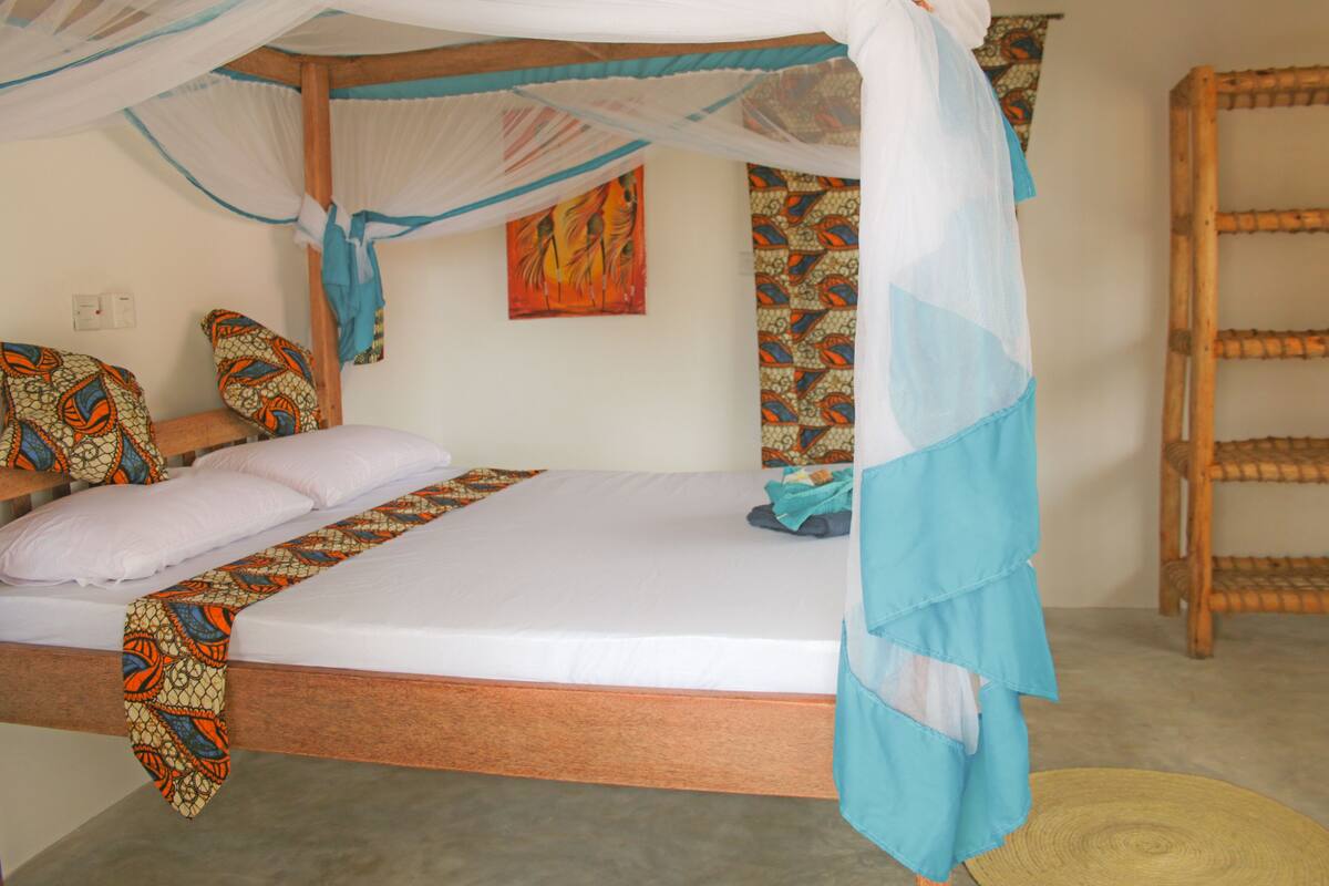 A bed with a canopy, patterned pillows, and a wall with a painting.