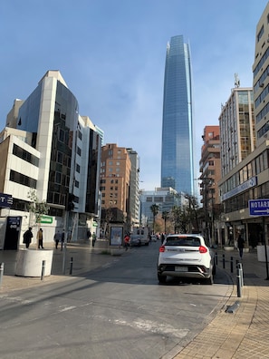 A city street with modern buildings, a tall skyscraper, and a white car parked on the side.