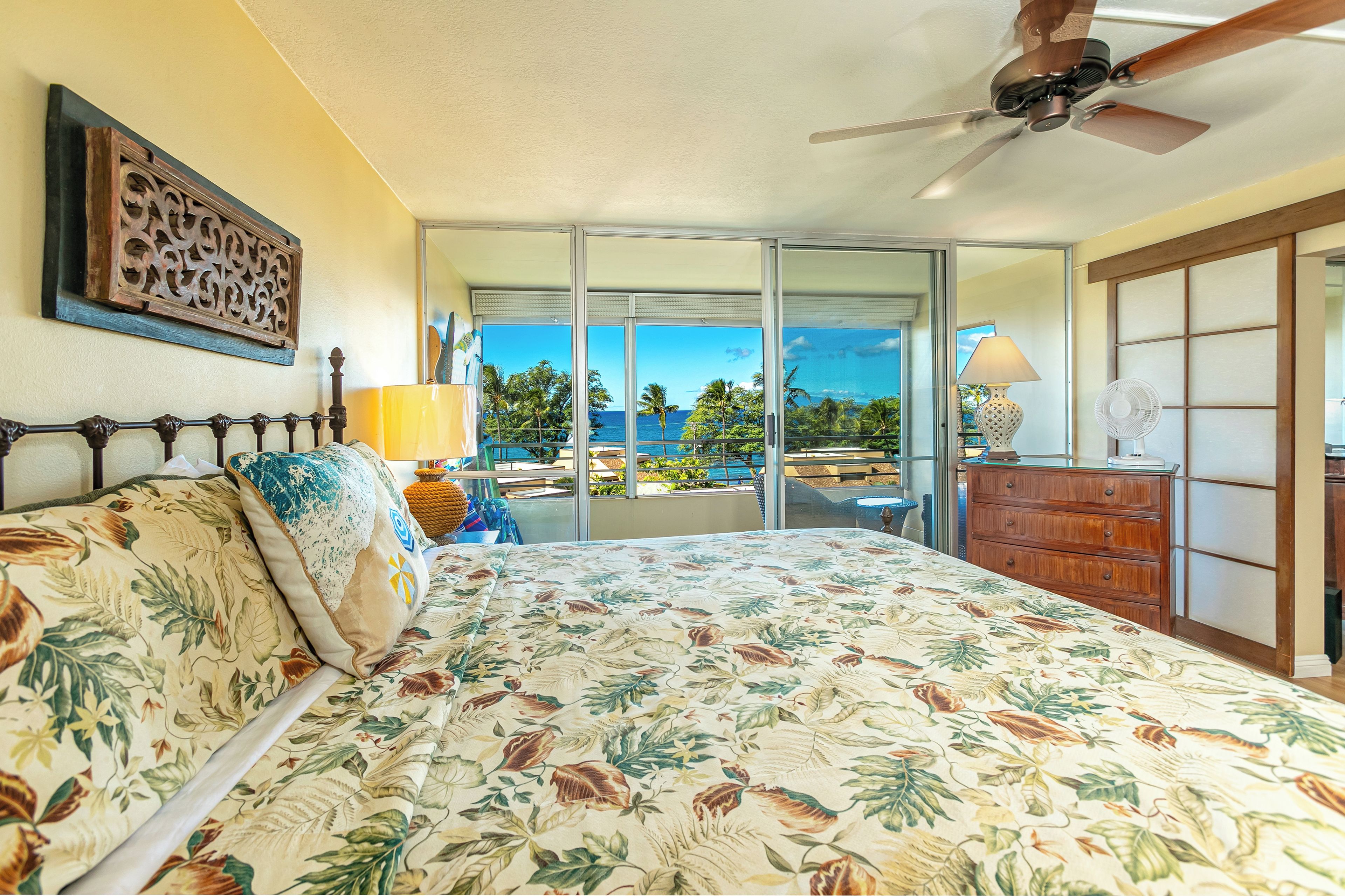 A bedroom with a bed, a ceiling fan, a dresser, and a view of the ocean.