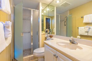A bathroom with a glass-enclosed shower, a white toilet, a sink with a mirror, and towels hanging on the wall.
