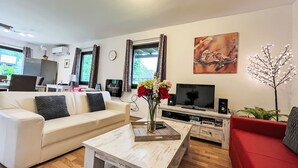 Un salon moderne avec un canapé, une table basse, un téléviseur et un divan rouge.