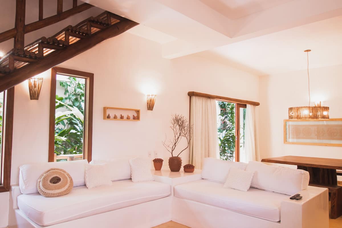 A modern living room with a white sectional sofa, a round woven rug, and a staircase with exposed wooden beams.