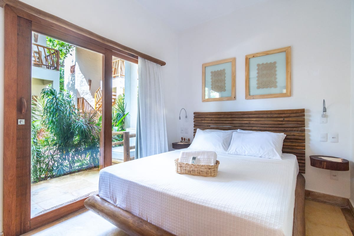 A bedroom with a bed, a nightstand, a wooden headboard, and a view of a garden through a sliding door.