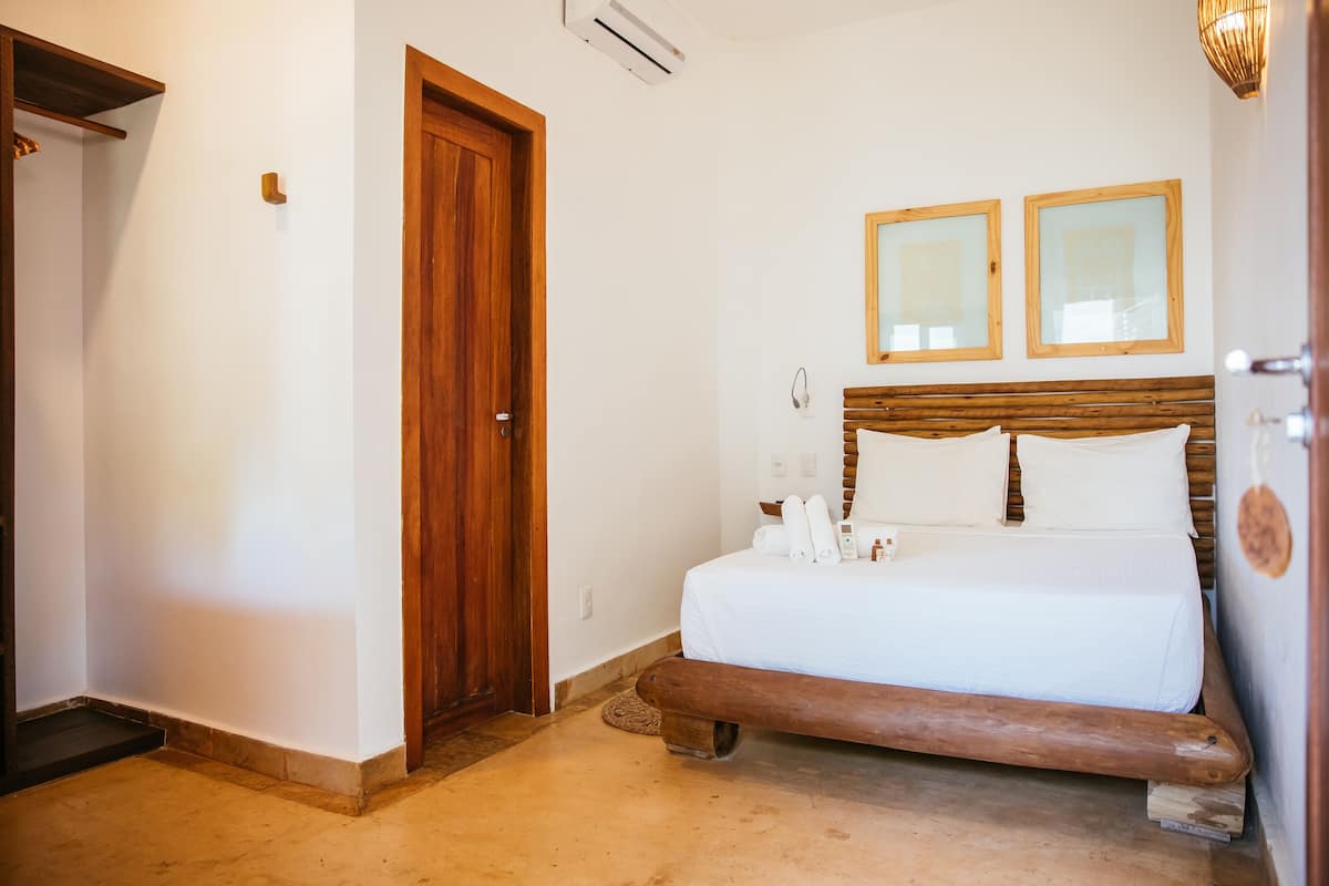 A bedroom with a wooden bed, a wooden bench, a door, and two framed mirrors on the wall.