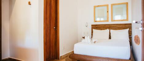 Un dormitorio con cama y banco de madera, una puerta y dos espejos enmarcados en la pared.