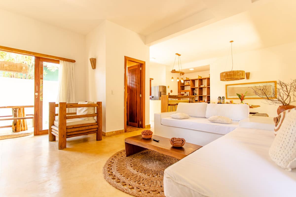 A spacious living area with a white sofa, wooden coffee table, and a large woven rug.