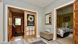 A hallway with a wooden door, a rug, a bench, and a bed in the adjacent room.