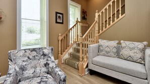 A living room with a staircase, a patterned armchair, and a grey sofa with patterned cushions.