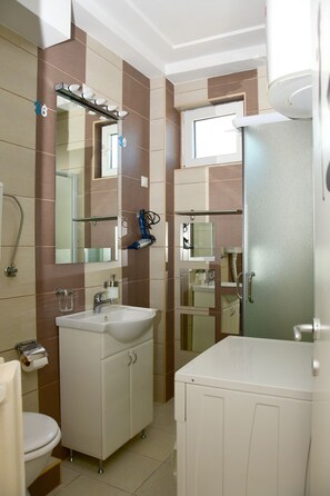 A modern bathroom with a white sink, mirror, and toilet. There are multiple shelves and a shower area.