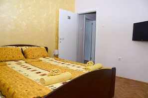 A hotel room with a bed, a door, a wall-mounted TV, and a light switch.
