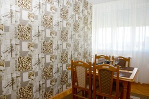 A dining area with a table set for four, wooden chairs, and a window with sheer curtains.