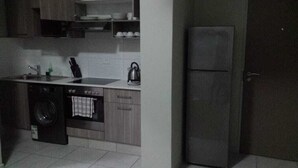 A compact kitchen with a washing machine, a kettle, and a refrigerator. - Apartmento Rosebank (Johannesburg)