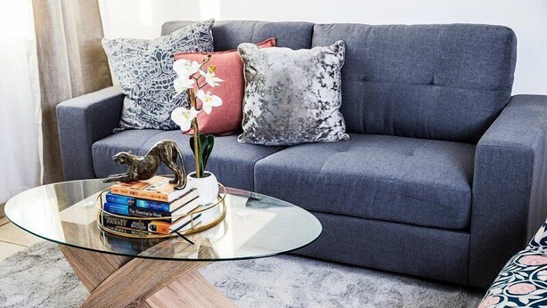 A living room with a grey sofa, a glass coffee table, and decorative pillows. - Apartmento Rosebank (Johannesburg)