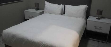 Una camera d'albergo standard con un letto singolo, due comodini e un tavolino da notte.