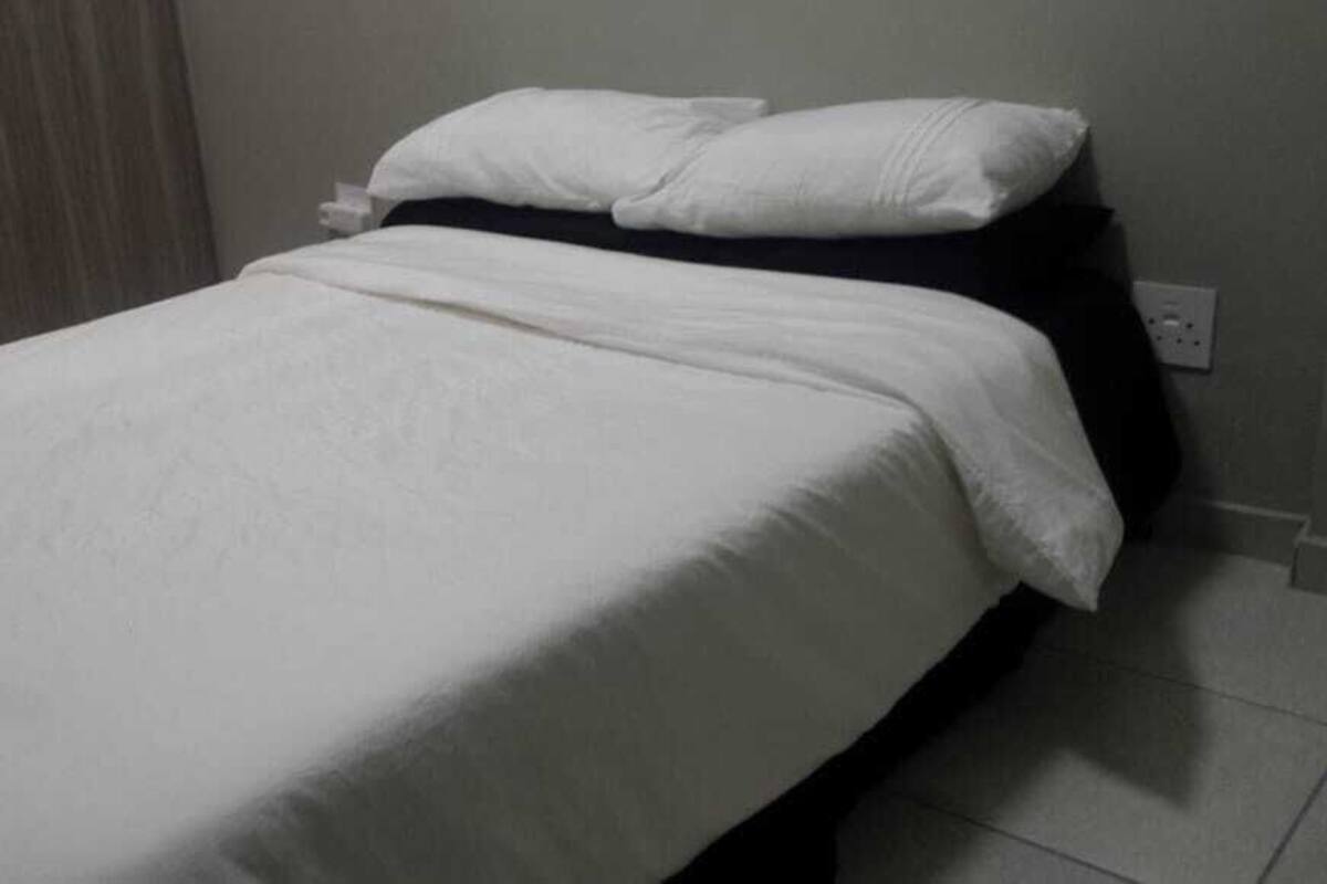 Ein Einzelbett mit weißer Bettwäsche in einem Raum mit schlichter Wand und einer Steckdose.