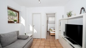 A compact living space with a grey sofa, a TV on a white cabinet, and a small table with a plant. - House Petra on the beach-sea (Cesarica)