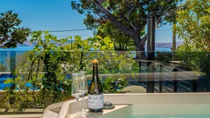 A hot tub with a bottle of wine and glasses, overlooking a body of water with trees and a clear sky. - House Petra on the beach-sea (Cesarica)