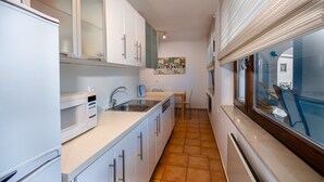 A narrow kitchen with white cabinets, a microwave, a sink, and a dining area with a table and chairs. - House Petra on the beach-sea (Cesarica)