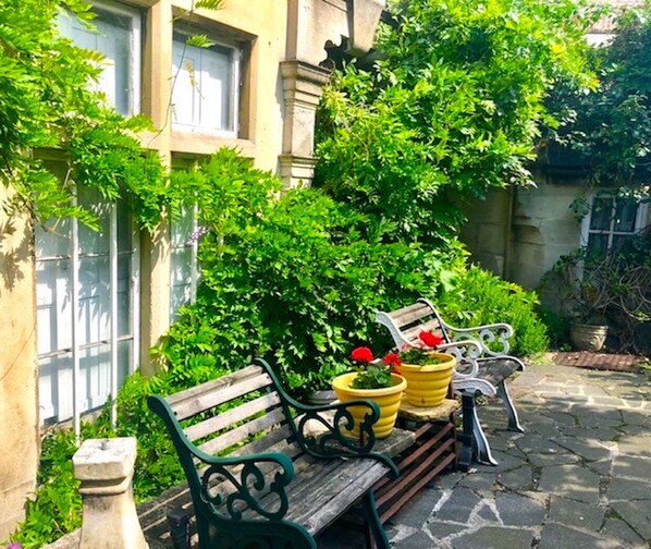 A wooden bench with potted plants and a white chair in a garden area with a stone pathway.