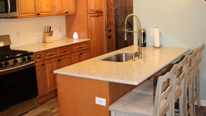 A kitchen with wooden cabinets, a built-in stove, a sink, and bar stools. - Our Cottage on Conesus Lake (Livonia)
