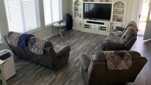 A living room with a grey sofa set, a TV on a white entertainment unit, and a dining area with a small table and chairs. - Our Cottage on Conesus Lake (Livonia)