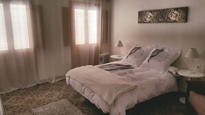 A neatly made bed with white linens, two bedside tables with lamps, a wall-mounted artwork, and a patterned rug on the floor. - Alojamiento Rural en el Centro de Zahara (Zahara de la Sierra)