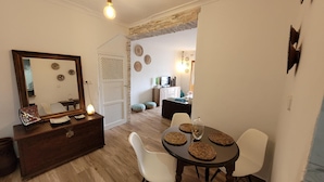 A dining area with a wooden table and chairs, a dresser with a mirror, and a doorway leading to another room with a TV and decorative items. - Alojamiento Rural en el Centro de Zahara (Zahara de la Sierra)
