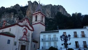 A church with a bell tower and a building with balconies in front of a rocky mountain backdrop.