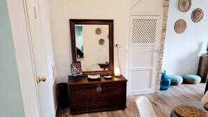 A room with a wooden dresser, a mirror, a white chair, a table with woven placemats, and a door with a decorative lattice. - Alojamiento Rural en el Centro de Zahara (Zahara de la Sierra)