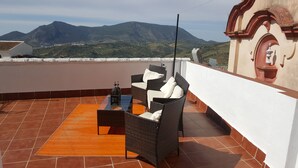 A terrace with wicker furniture, a table, and a view of mountains. - Alojamiento Rural en el Centro de Zahara (Zahara de la Sierra)