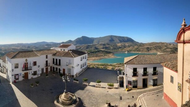 A plaza with white buildings, a fountain, and a view of a lake and mountains. - Alojamiento Rural en el Centro de Zahara (Zahara de la Sierra)
