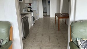 Ett modernt kök med vita skåp, en mikrovågsugn, ett kylskåp och en diskmaskin. I förgrunden står ett matbord med en stol.