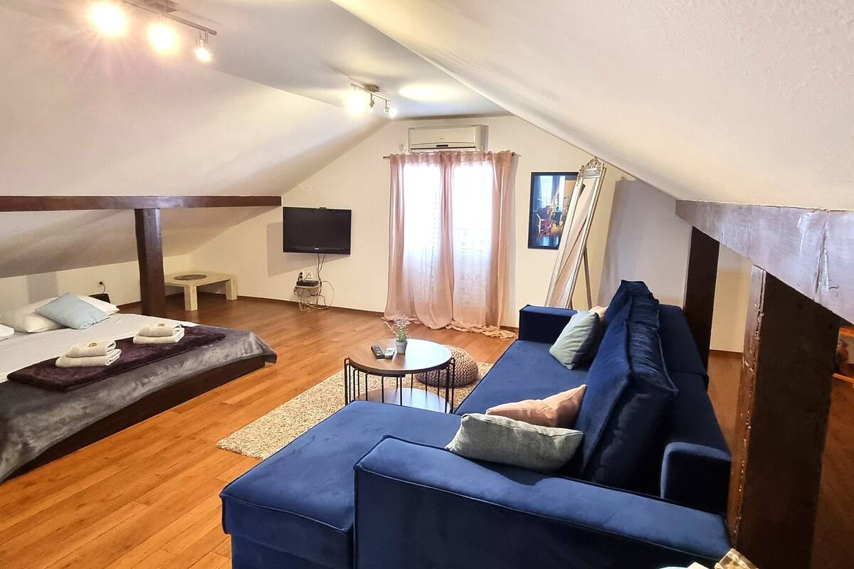 A cozy loft bedroom with a large bed, a blue sofa, and a TV.