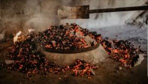 A large pile of coal or charcoal with a metal tool nearby, possibly for handling or processing.