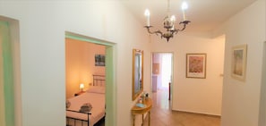 A hallway with a bed, a mirror, and a chandelier.