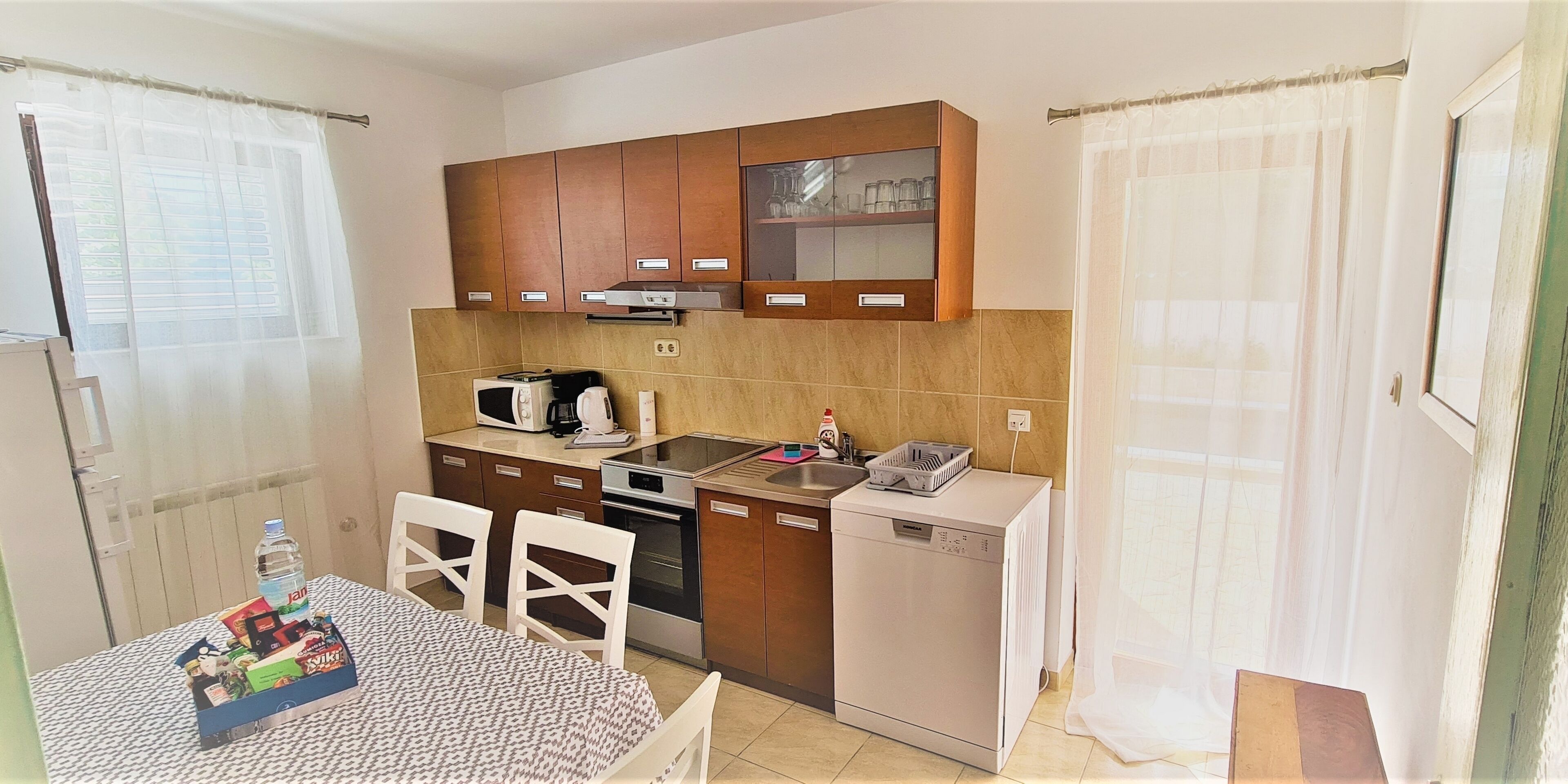 A compact kitchen with a microwave, toaster, and dishwasher. There is a dining table with chairs and a small refrigerator.