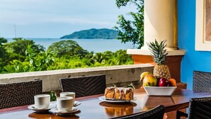 Une table à manger avec vue sur la mer, un ananas et un saladier rempli de fruits.