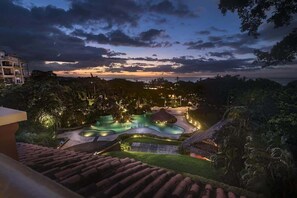 A resort with a swimming pool, lush greenery, and a view of the ocean at dusk.