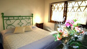 A bedroom with a green metal headboard, a bed with patterned bedding, a bedside table with a lamp, and a window with a view of greenery. - single house in tuscany (SIENA)