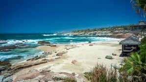 A beach with rocky shoreline, clear blue water, and a thatched-roof structure.