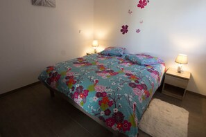 Une chambre à coucher avec une couvre-lit à motifs floraux, deux lampes de chevet, un tapis blanc et une décoration murale représentant des fleurs et des papillons.