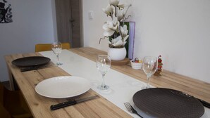 Ruokapöytä on katettu lautasilla, aterimilla ja viinilaseilla. Pöydällä on myös maljakko, jossa on kukkia, sekä pieni koriste-esine.