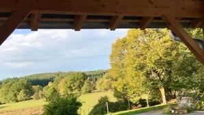 Blick von unter einer Holzkonstruktion auf eine grüne Landschaft mit Bäumen und Hügeln.