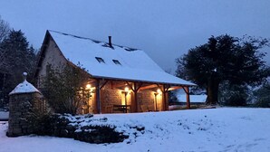 Eine Steinhütte mit schneebedecktem Dach und einer Holzterrasse, umgeben von Schnee.