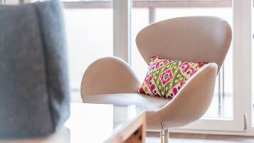 Une chaise moderne avec un coussin coloré, placée dans une pièce lumineuse dotée d’une grande fenêtre.