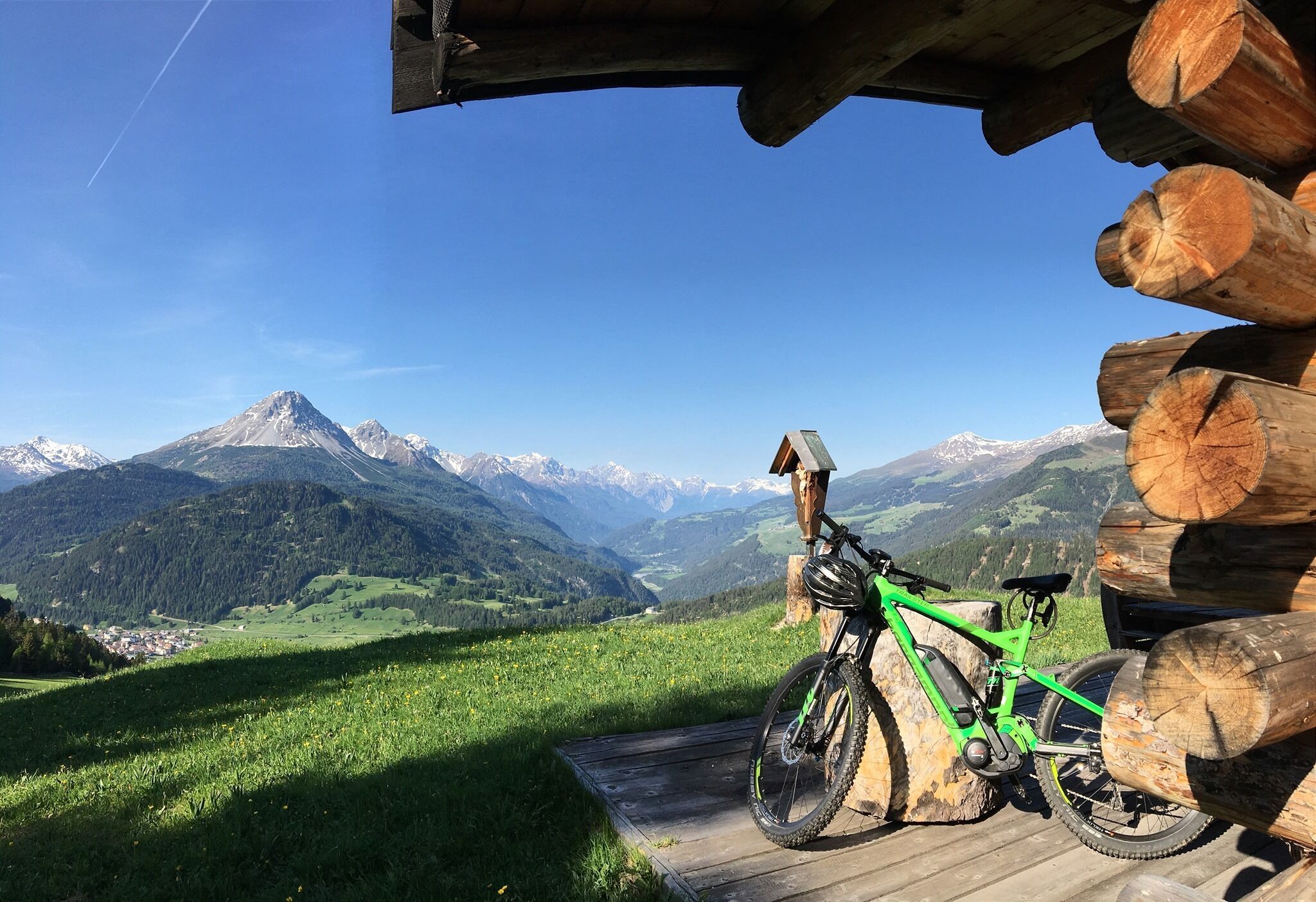A mountain bike parked on a wooden deck with a scenic view of snow-capped mountains and a clear sky.