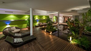 A modern outdoor lounge area with wooden flooring, green walls, and seating arrangements. - Hotel Naudererhof (Nauders)