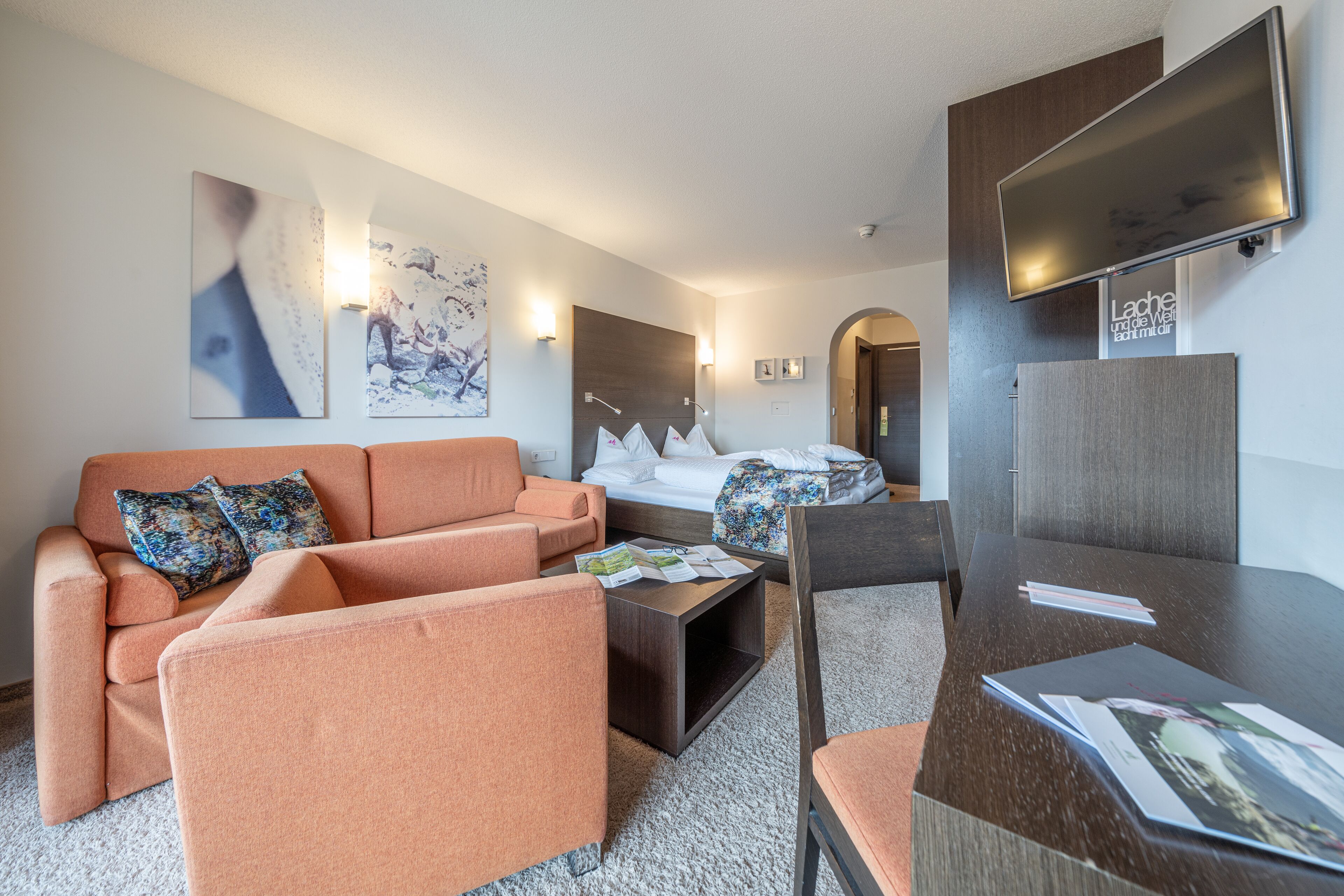 Una habitación de hotel moderna con sofá, sillón y un escritorio con documentos.