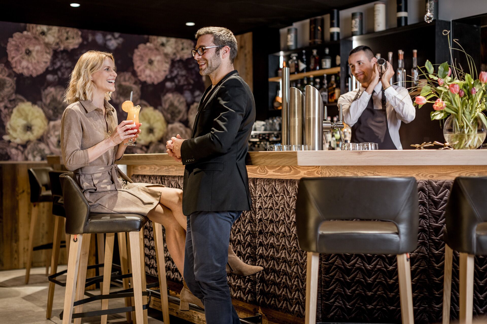 A bar area with wooden stools, a counter with bar tools, and a floral wall backdrop.