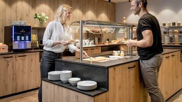 Mostrador de buffet con vitrina de vidrio, platos y una máquina de café.